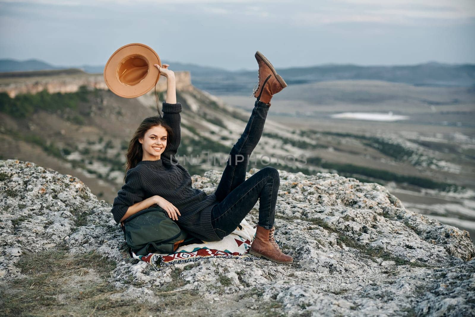 carefree woman in straw hat relaxing on rocky ledge with legs raised in air by Vichizh