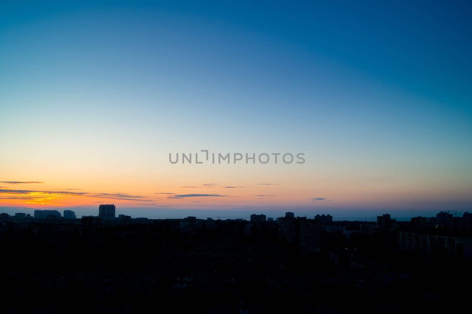Five minutes before sunrise over the city. Almost clear sky with a light area above the horizon. Silhouettes of buildings in backlight