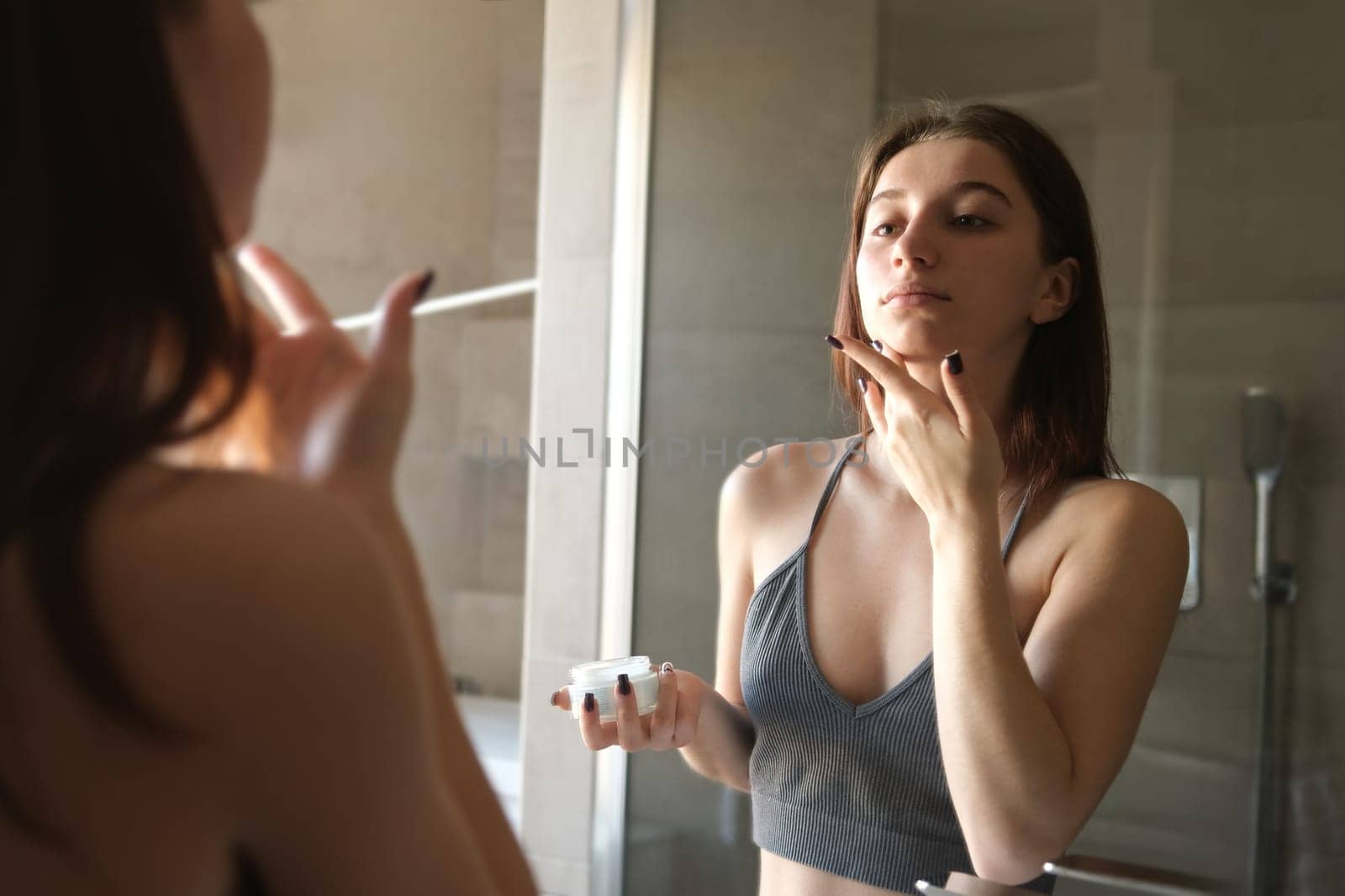Young Girl Applying Skin Cream On Her Face And Body In Front Of A Bathroom Mirror