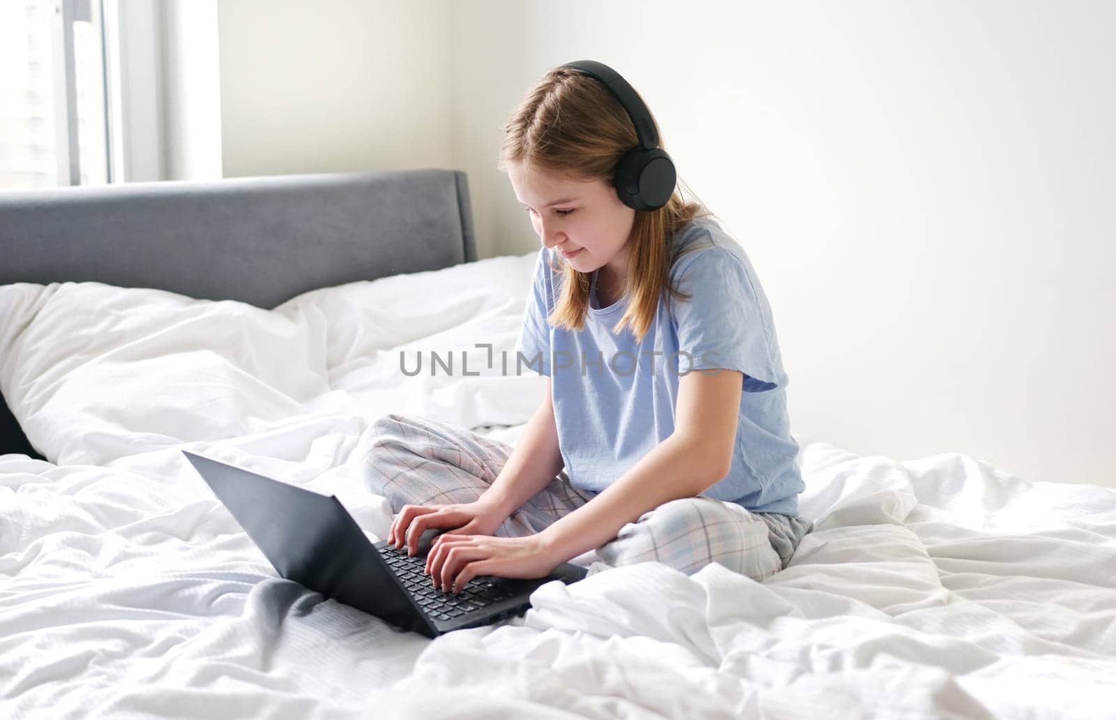 Sweet Young Girl Talking To Her Friends On Social Media Using Her Laptop While Sitting On Her Bed