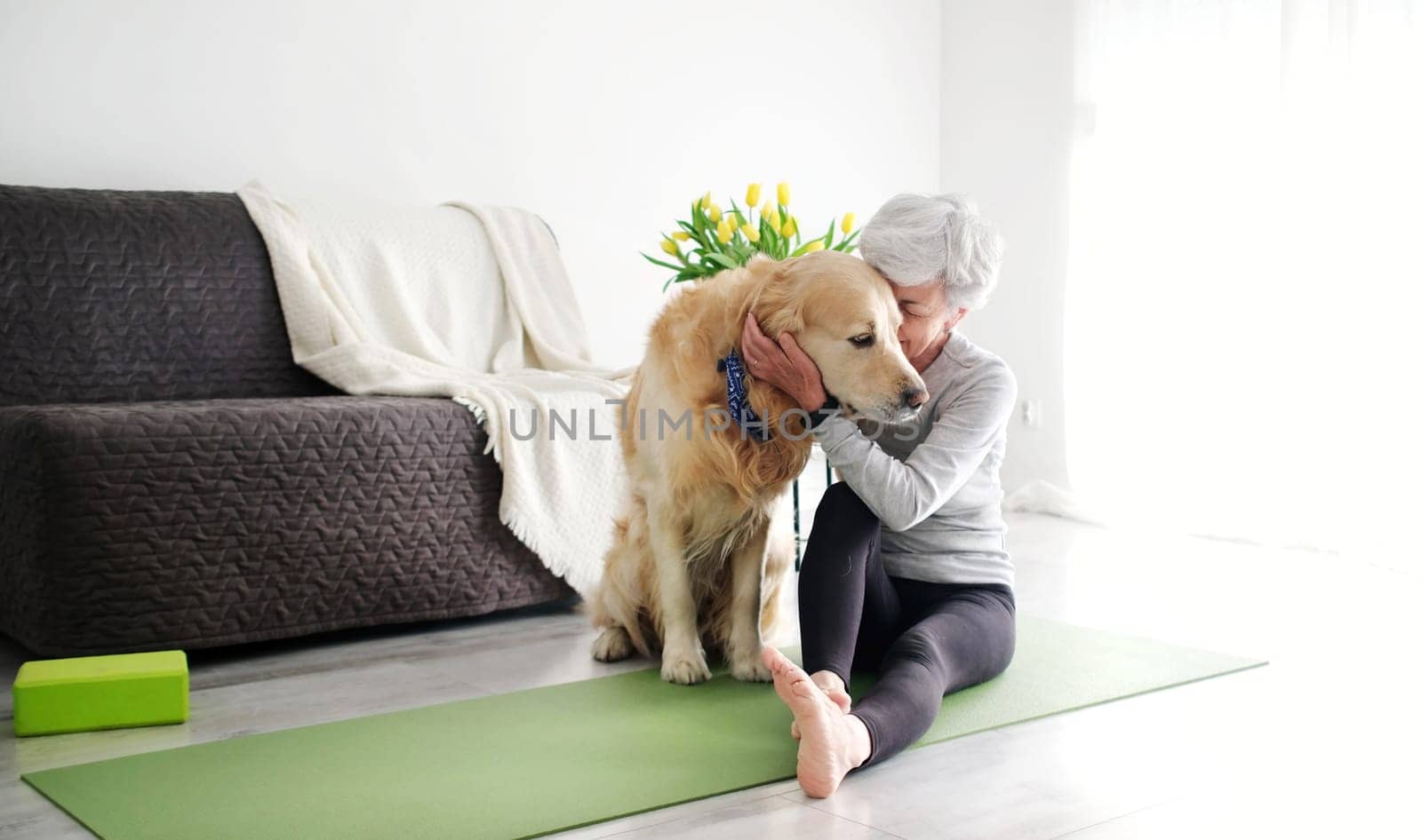 Elderly Woman With A Smile, Actively Hugging Her Dog On A Yoga Mat At Home