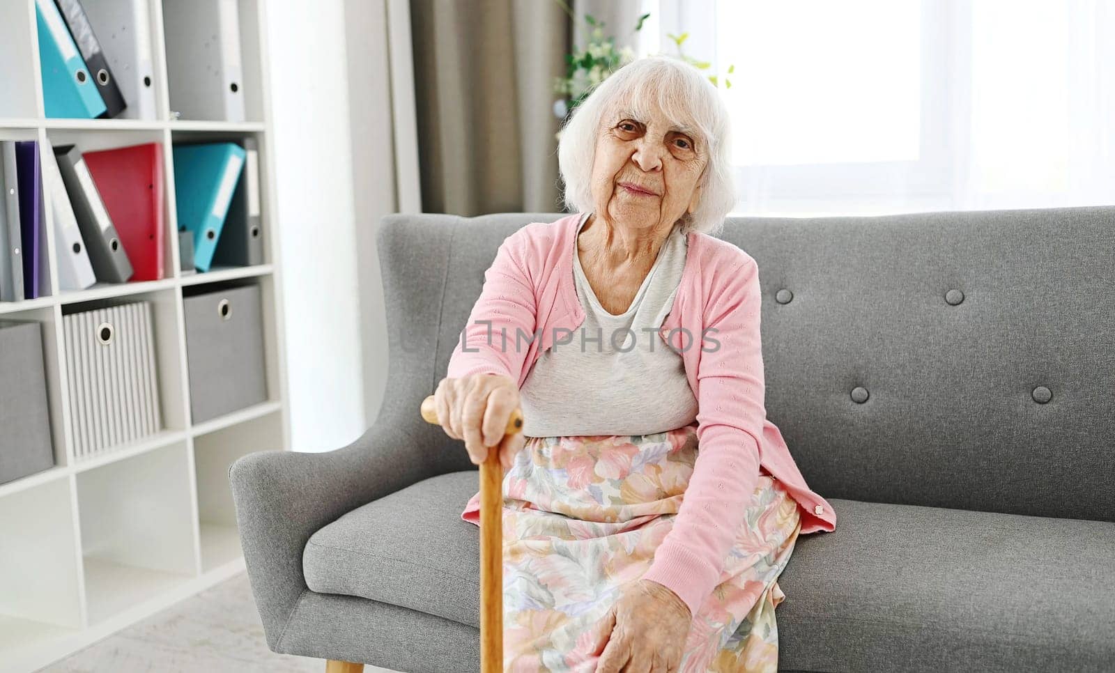 Elderly Woman Sitting On A Living Room Sofa With Cane Laughing And Looking Into The Camera