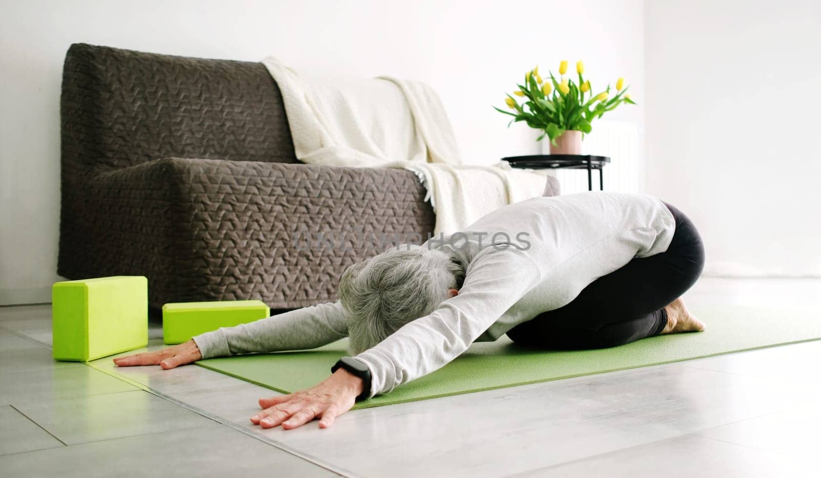 Appealing Elderly Woman With Grey Hair Doing Yoga, Resting In Child Pose