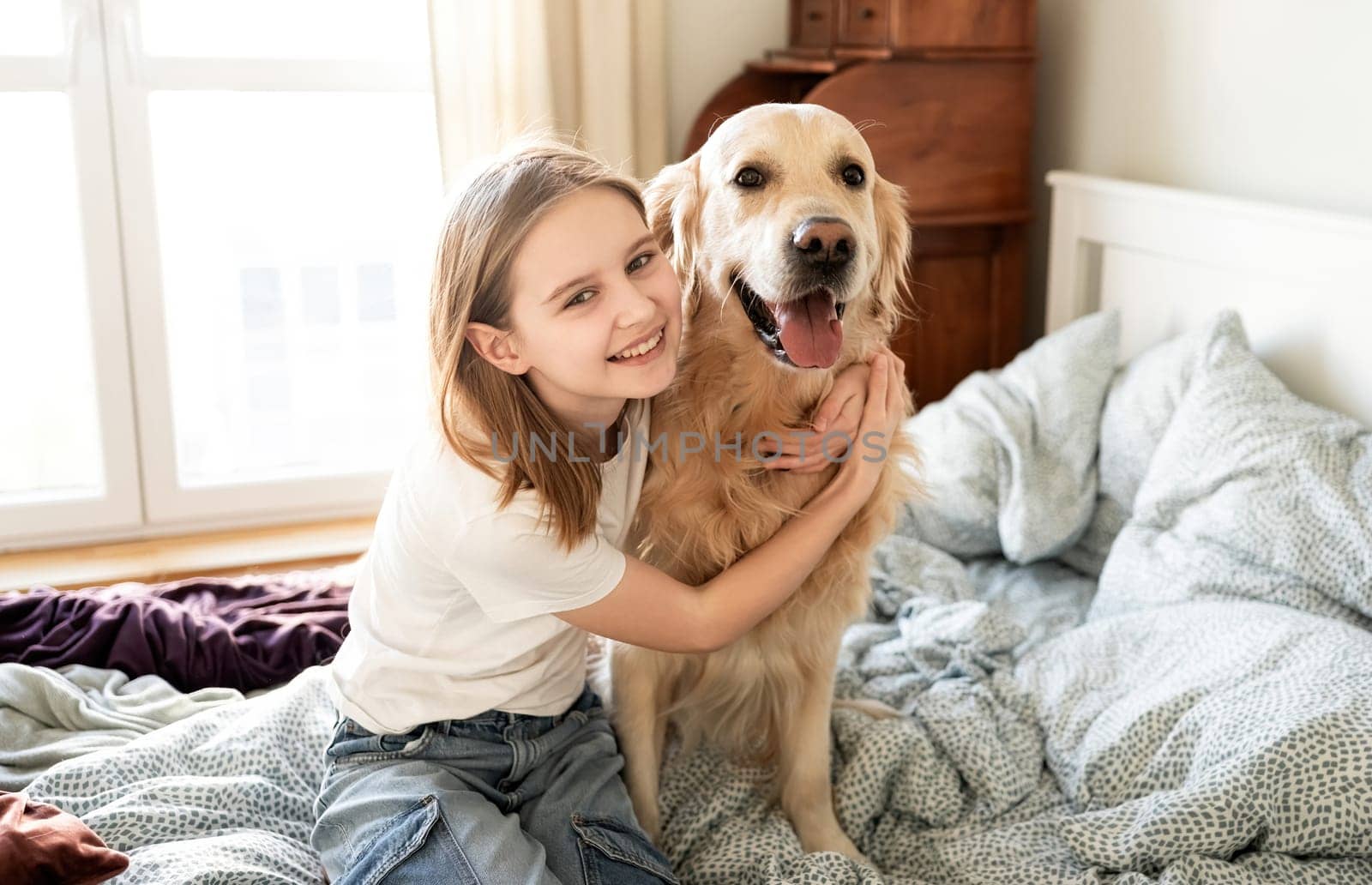 Joyful Little Girl Hugging Golden Retriever Dog And Looking Into The Cameara