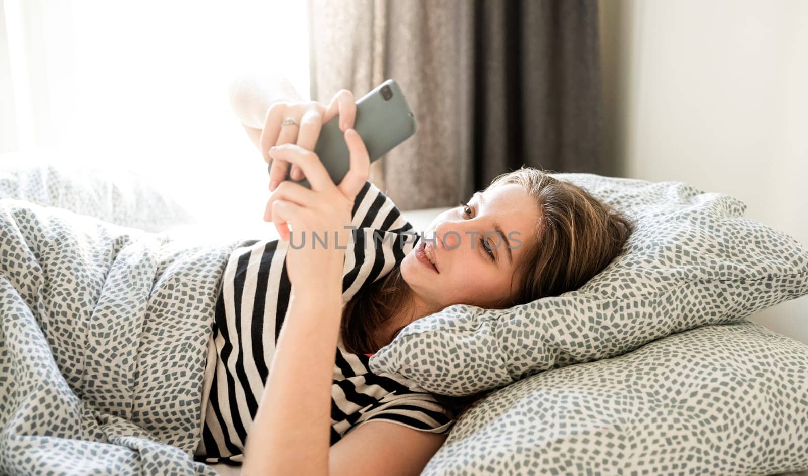 Teenage Girl Typing Message On A Smartphone Lying On A Bed