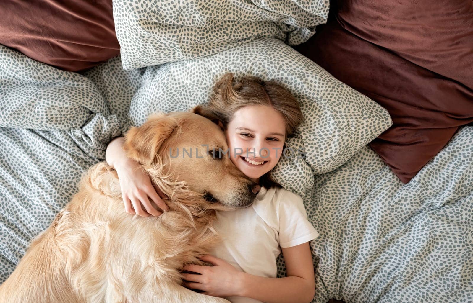 Happy Little Girl Hugging Dog And Smiling Lying On A Bed