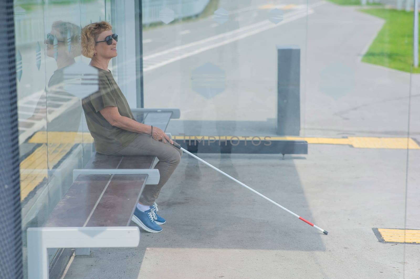 An elderly blind woman is waiting for transport at a bus stop