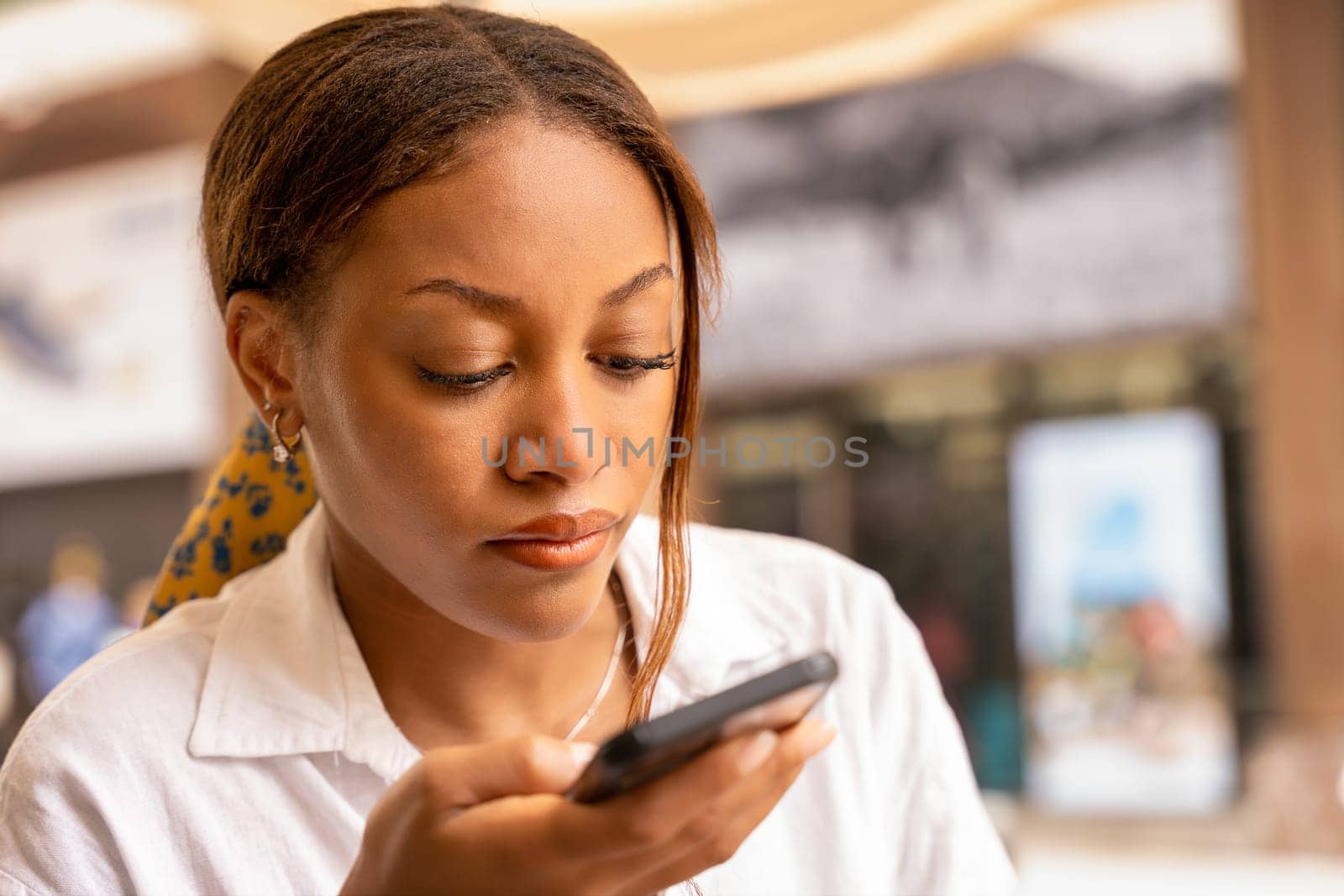 A woman is engrossed, scrolling on her cellphone in the vibrant city of Bilbao, surrounded by urban hustle and bustle.