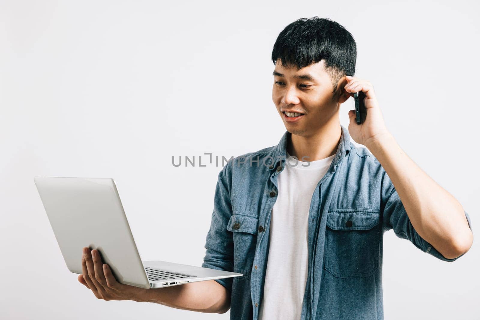 Portrait Asian smiling young man holding a laptop and talking on cell mobile phone studio shot isolated white background, Happy excited lifestyle businessman using computer and talking on smartphone