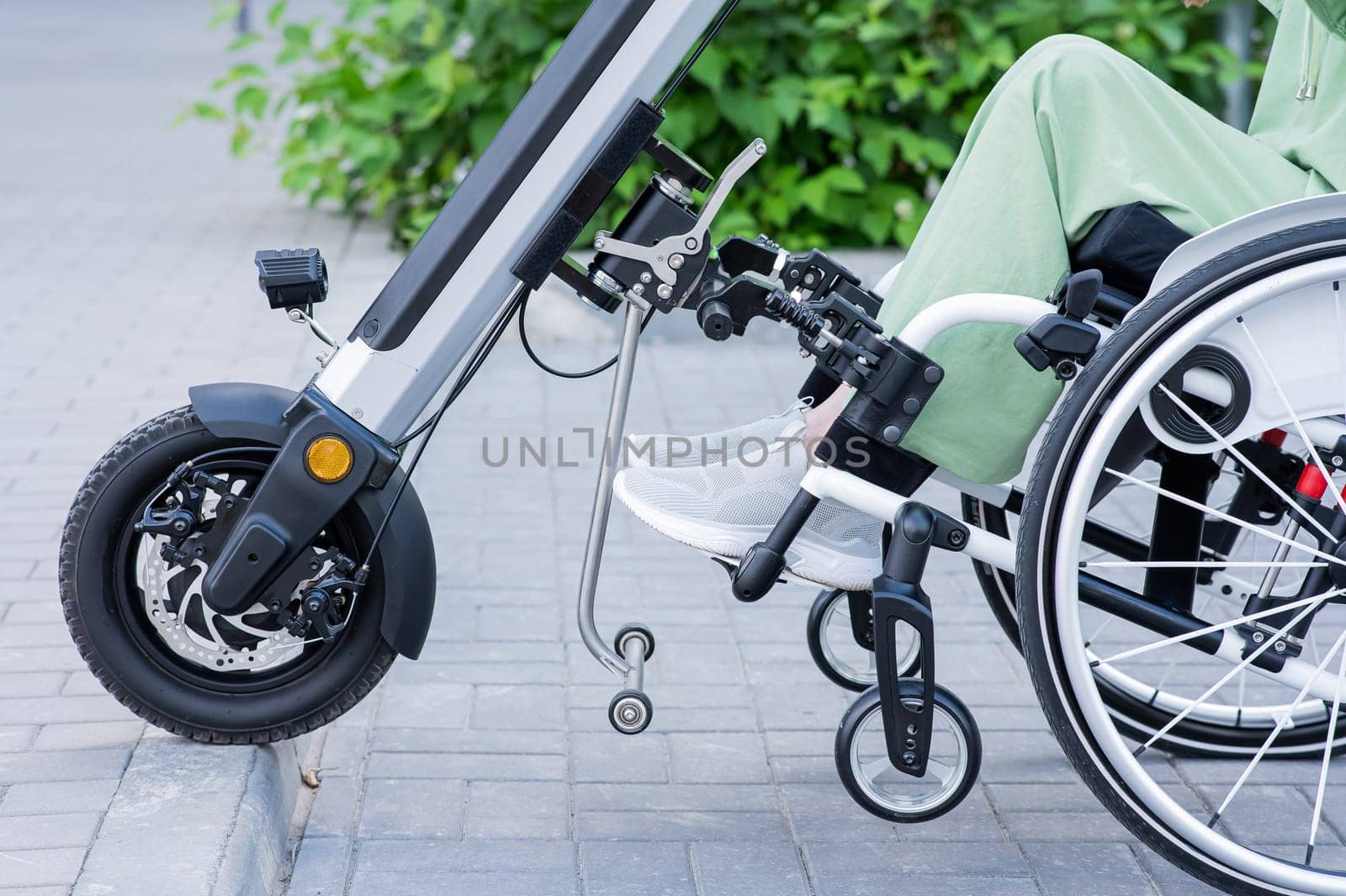 A faceless woman in a wheelchair with an assistive device for manual control. Electric handbike