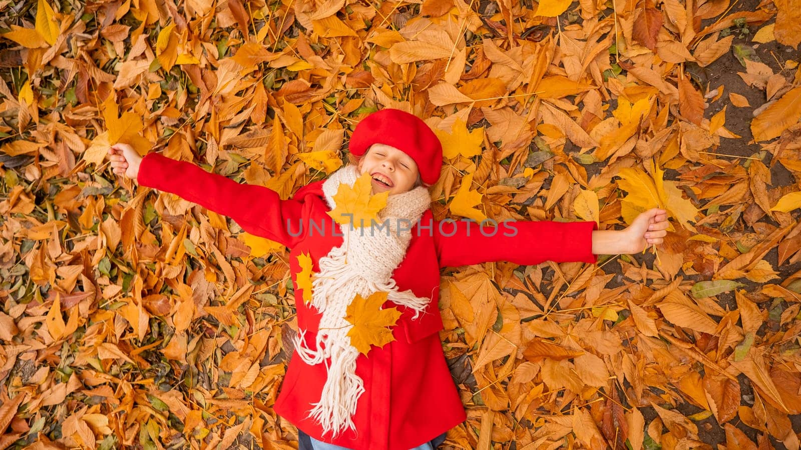 An overhead view of a caucasian girl in a red coat and beret lies on yellow foliage. Walk in the park in autumn