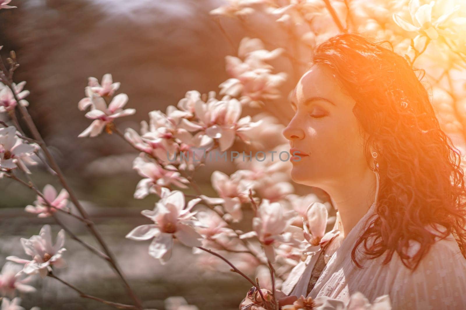 Magnolia park woman. Stylish woman in a hat stands near the magnolia bush in the park. Dressed in white corset pants and posing for the camera. by Matiunina