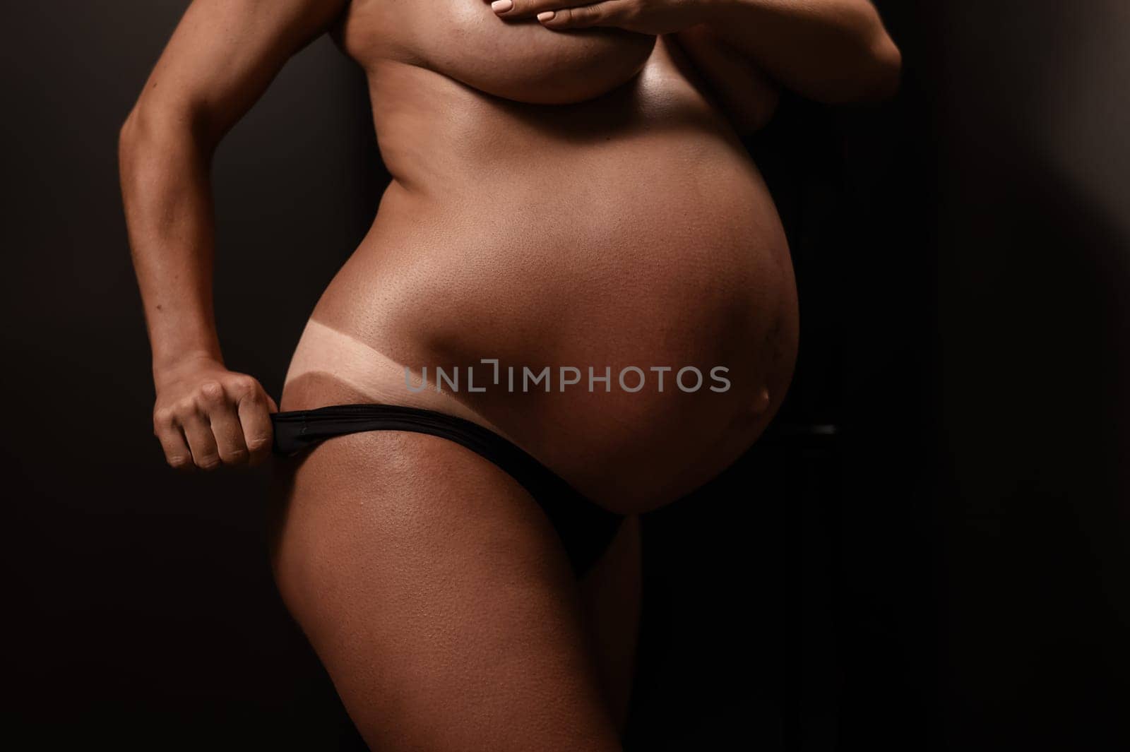 Pregnant woman pulls back her panties showing instant tan. Vertical photo