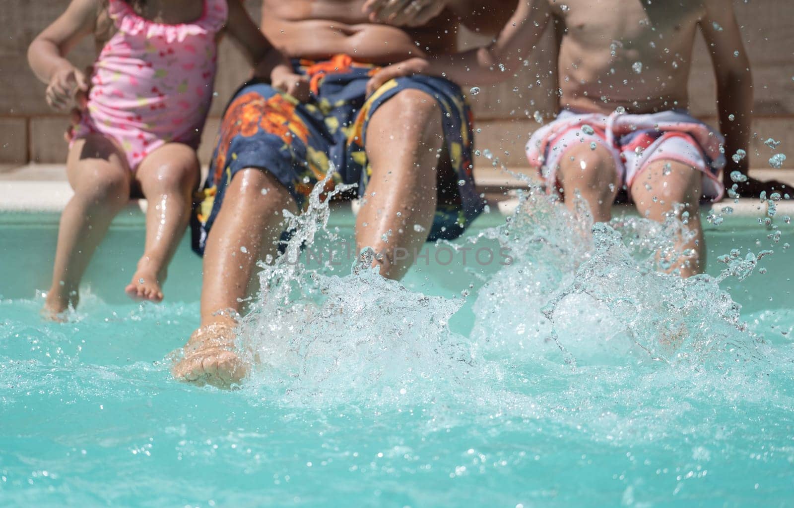 Unrecognizable family splashing water at the edge of the pool. Summer holidays concept.