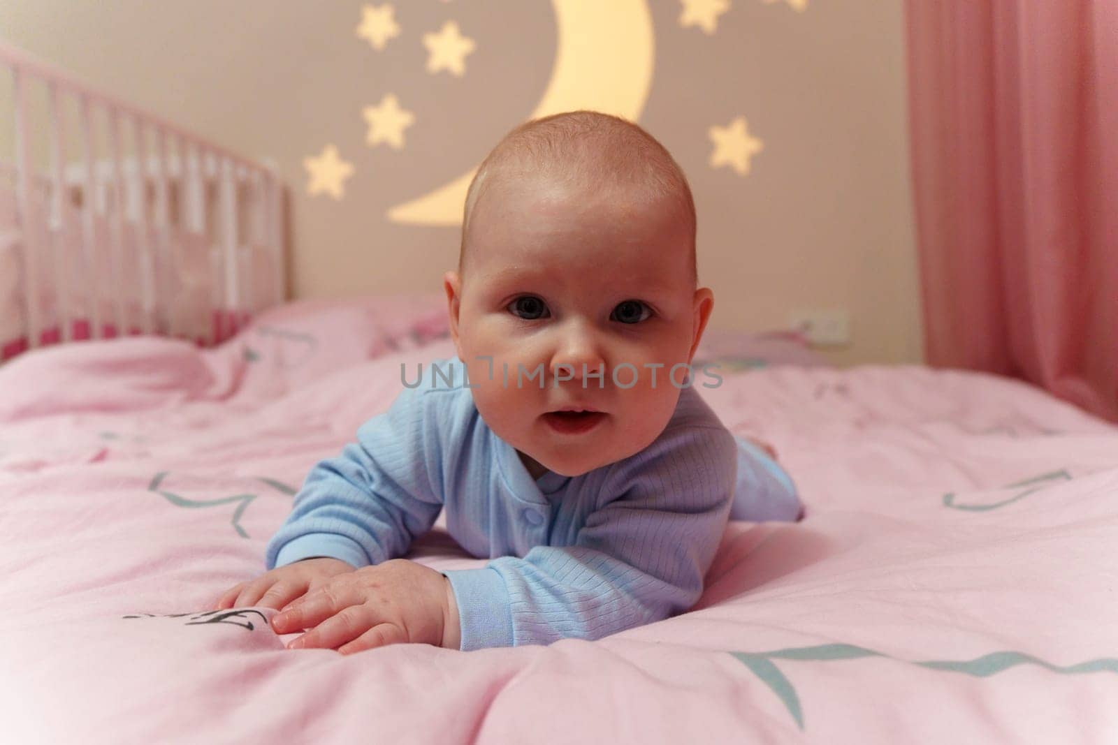 Peaceful baby lays on a bed next to a crib, surrounded by a cozy atmosphere and gentle tones.