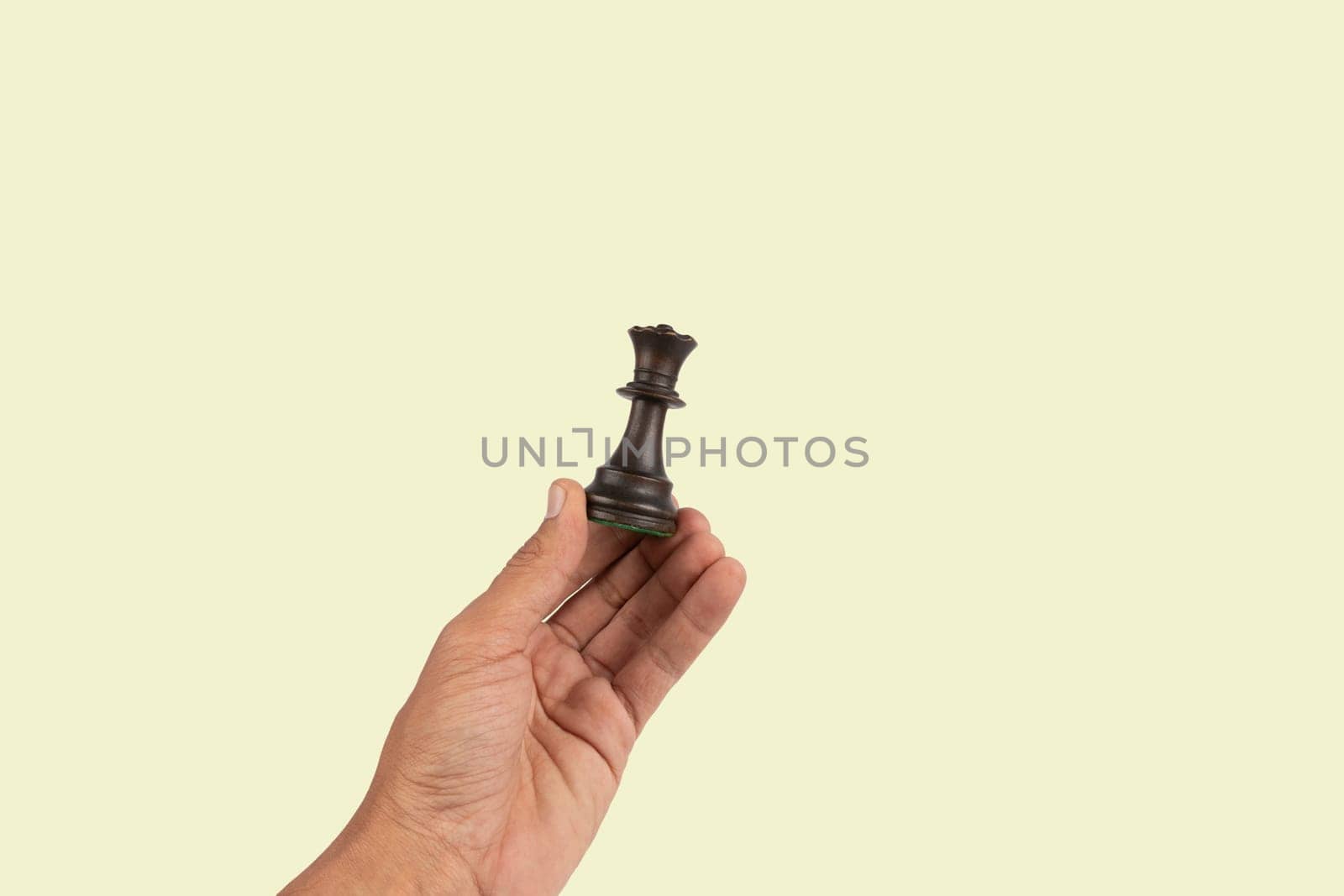 Black male hand holding a black queen chess figure isolated on green background by TropicalNinjaStudio