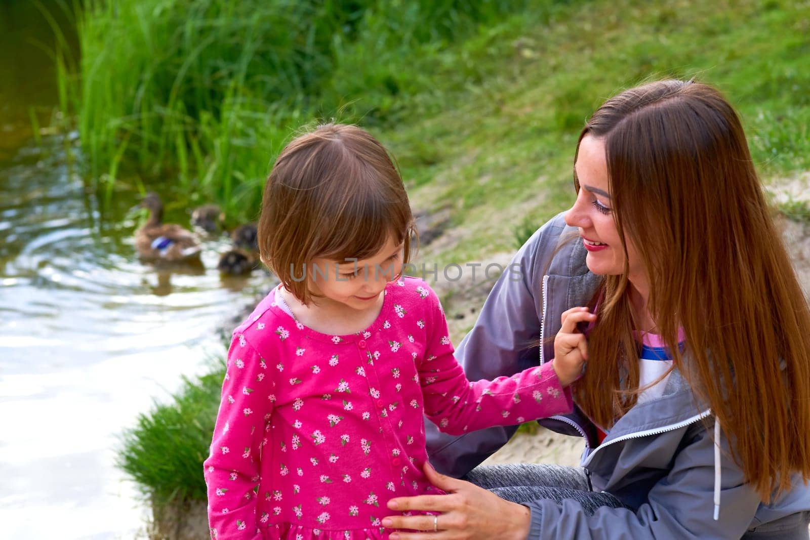 Charming mother and daughter on the shore of a pond with ducks by jovani68