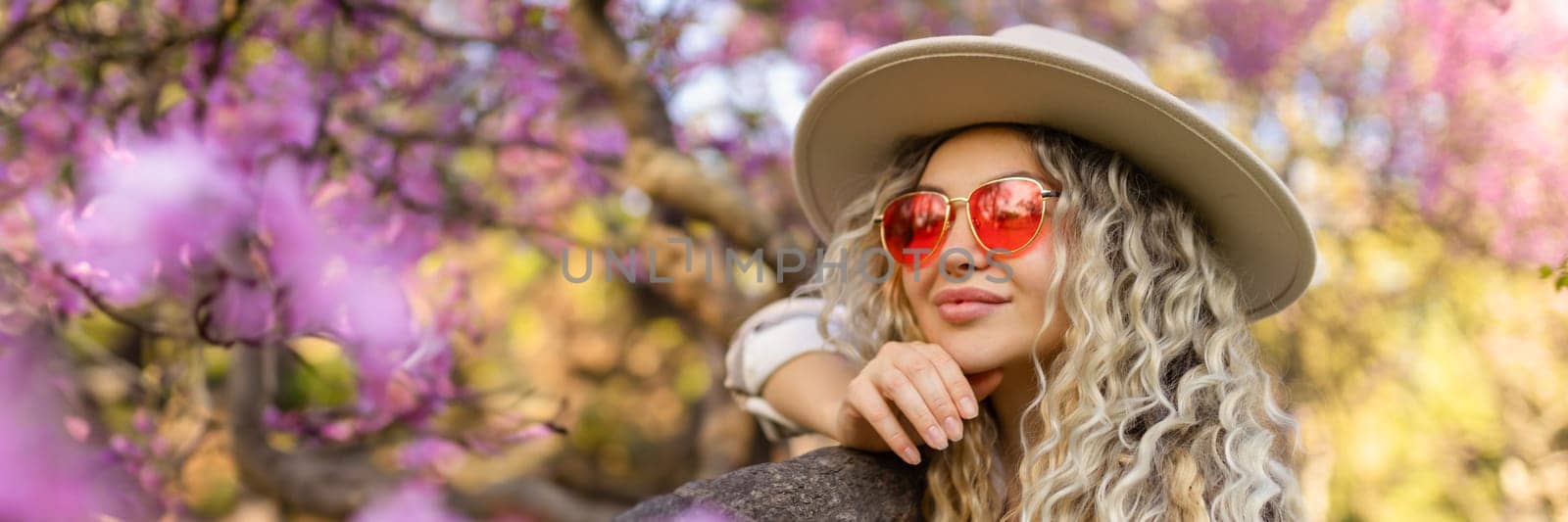 Beautiful woman in sunglasses near blossoming tree on spring day, space for text banner by malyshph