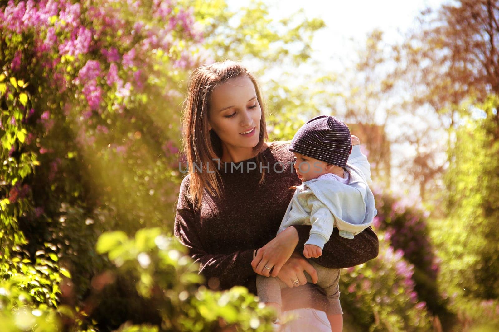 A mother holds her son in her arms. High quality photo. Mother and child in the rays of the sun among the blooming lilacs.