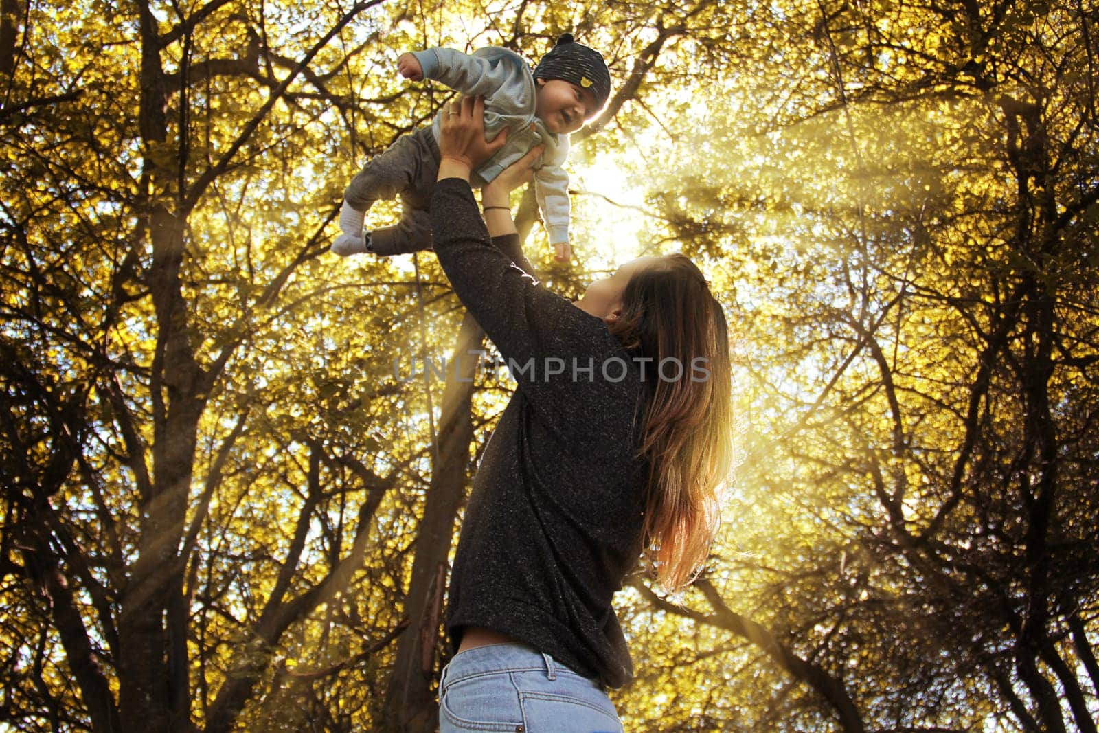 Mother holding her son in her arms. High quality photo. Portrait of mother and child in the rays of the sun among the trees