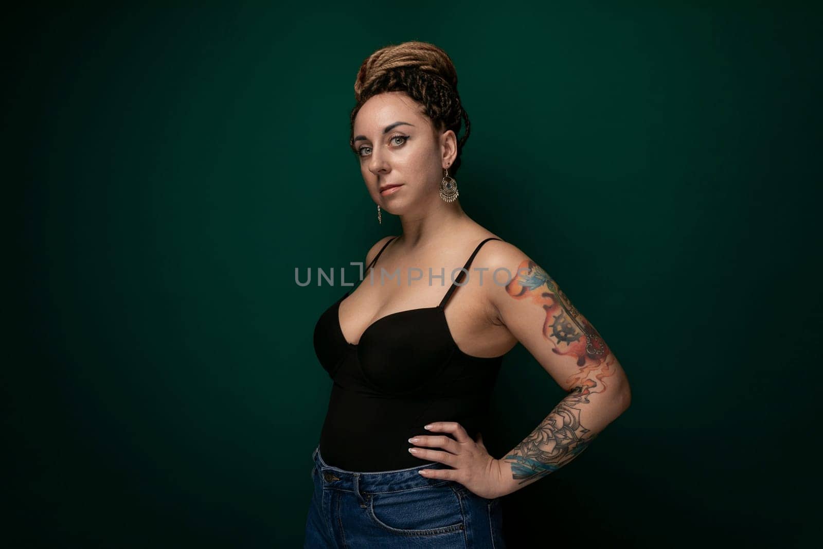 A woman is standing in a black tank top, striking a pose for a camera. Her arms are slightly raised, and she is smiling. The background is nondescript.