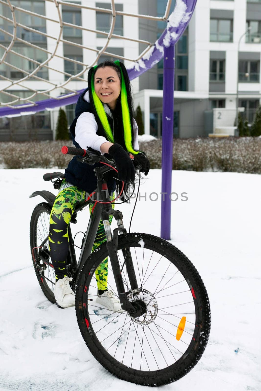 A woman is seated on top of a stationary bike in a snowy landscape. She appears to be taking a break from riding and is bundled up in winter clothing.