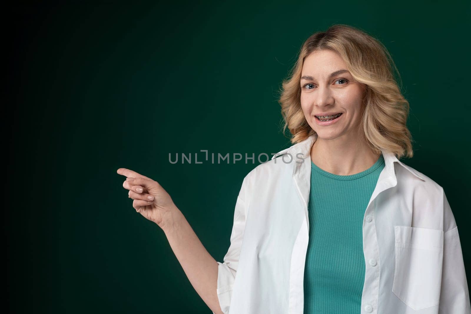 A woman wearing a white jacket standing and pointing at an object or direction. She appears focused and engaged in explaining or indicating something to others.