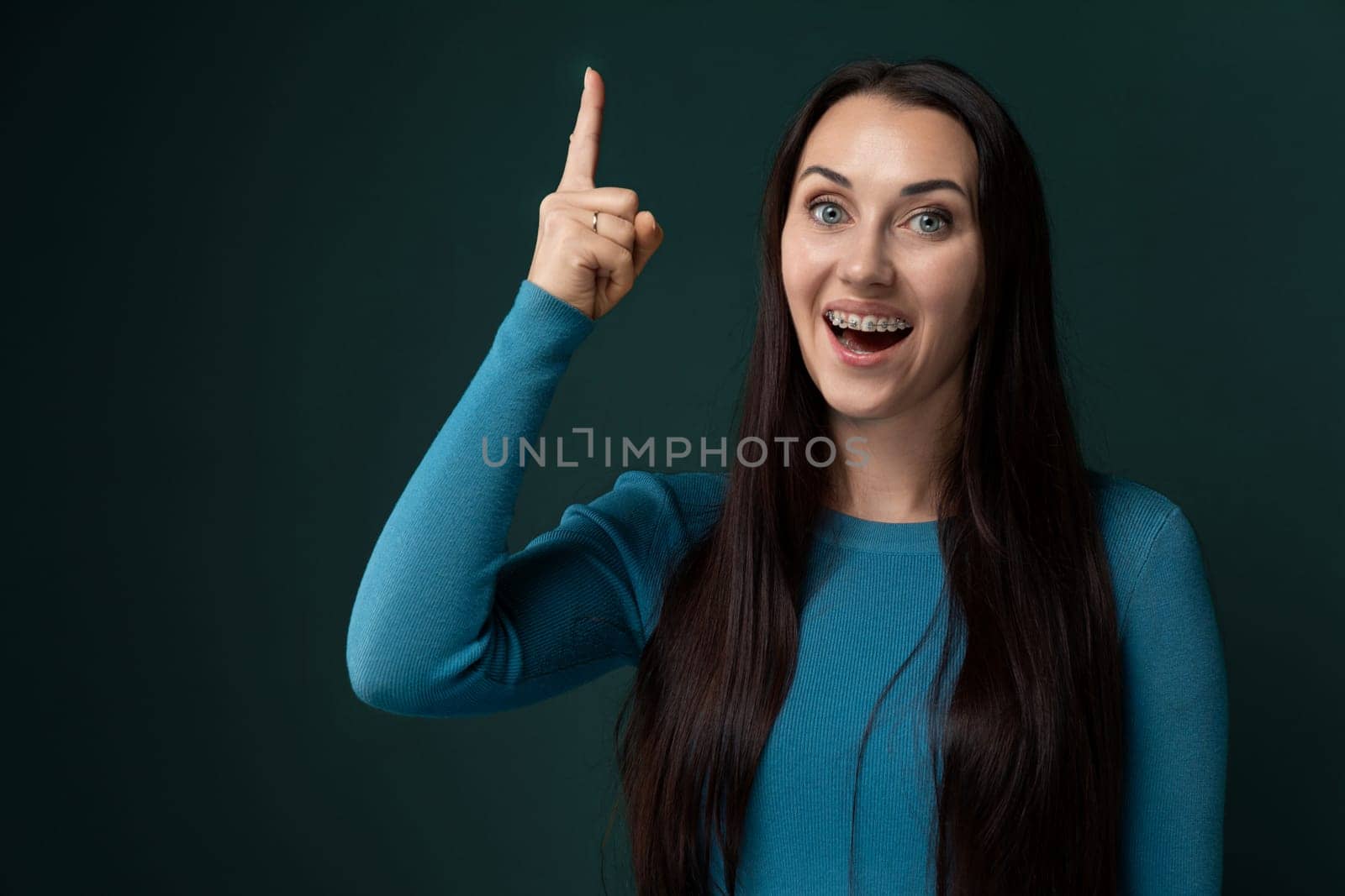 A woman with long black hair is pointing to the side in the image. She is dressed in casual attire and appears to be gesturing towards something off-camera. Her hair is flowing and shiny, drawing attention to her action.