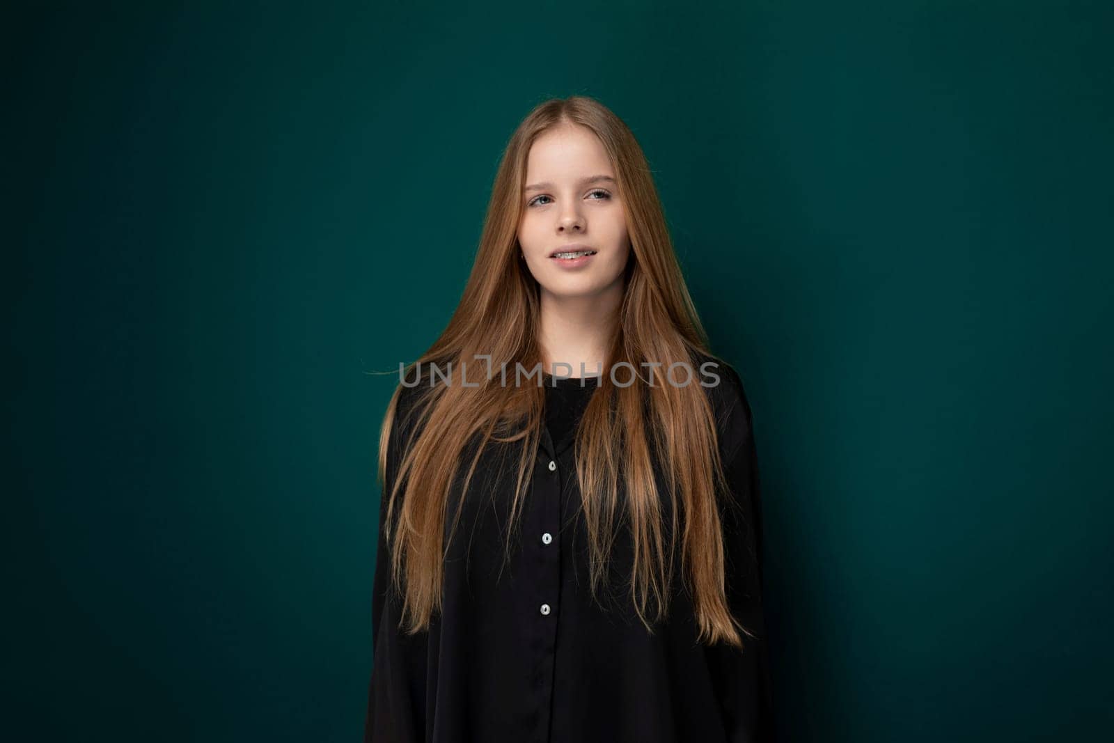 A young girl stands in front of a vibrant green wall, her posture confident and gaze focused. The stark contrast between her figure and the wall creates a striking visual impact, highlighting her presence in the scene.