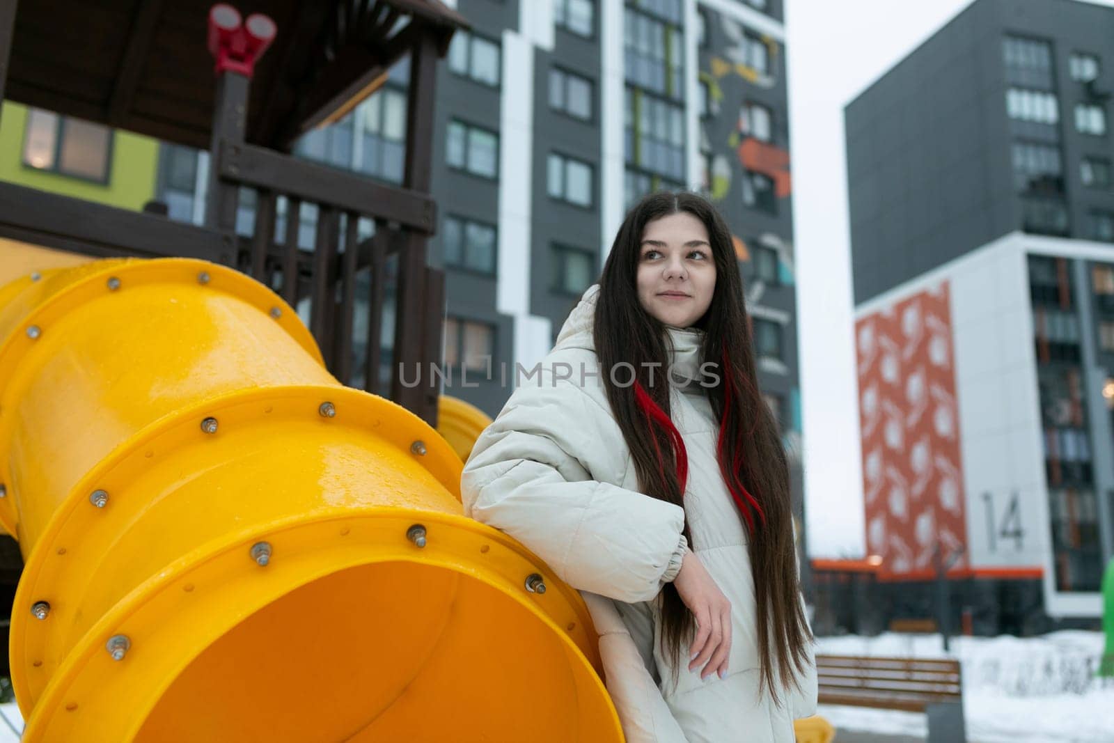 A woman is standing beside a massive yellow structure, looking up at it with a curious expression. The object seems to dominate the scene, showcasing its size and vibrant color.