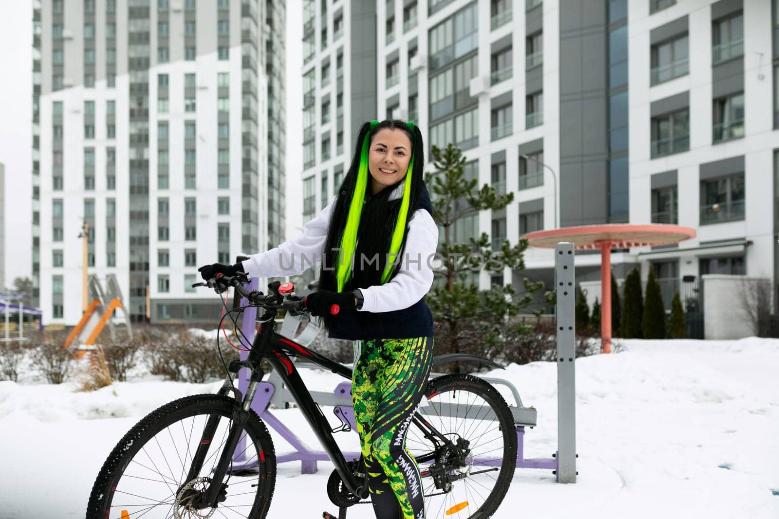 A woman is standing next to a bicycle in a snow-covered landscape. She is dressed in winter clothing and appears to be examining the bike.