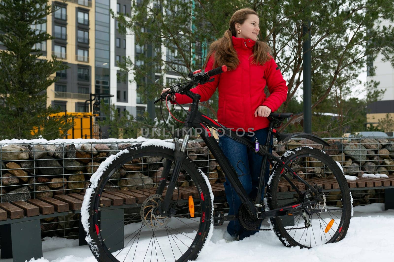 Pretty young woman in a winter jacket stands with a bicycle on the street.