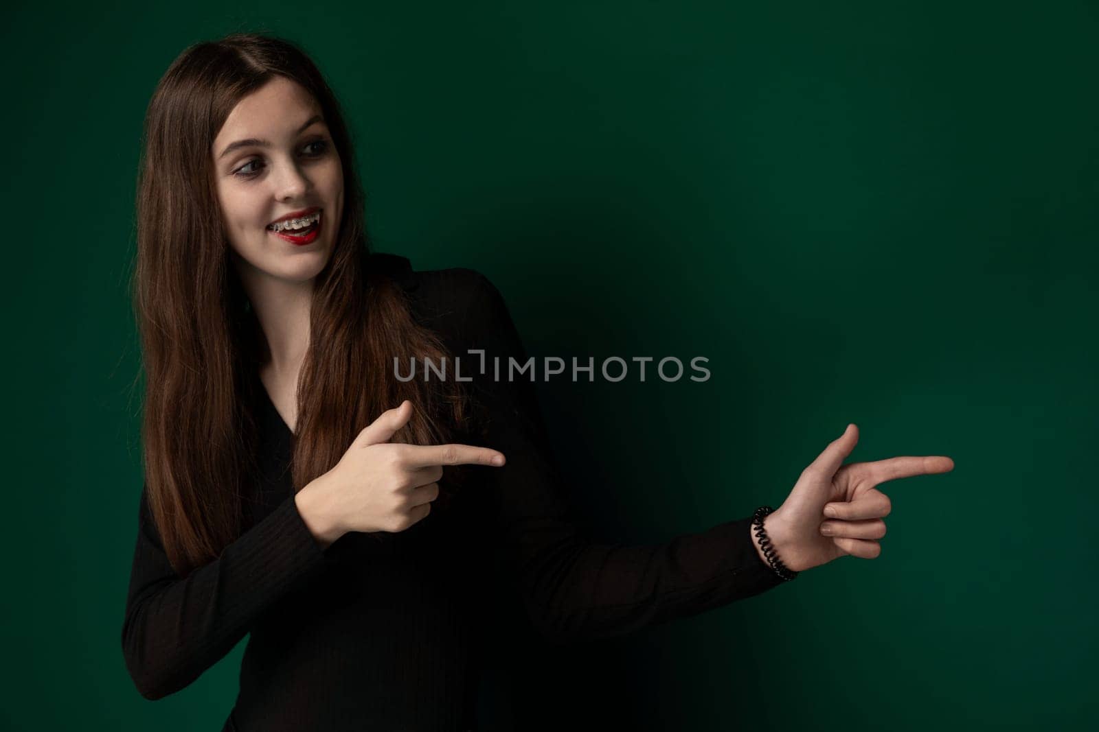 A woman with flowing long hair extends her arm and points at an unseen object with a focused expression. Her gesture appears confident and purposeful, drawing attention to whatever has caught her eye.