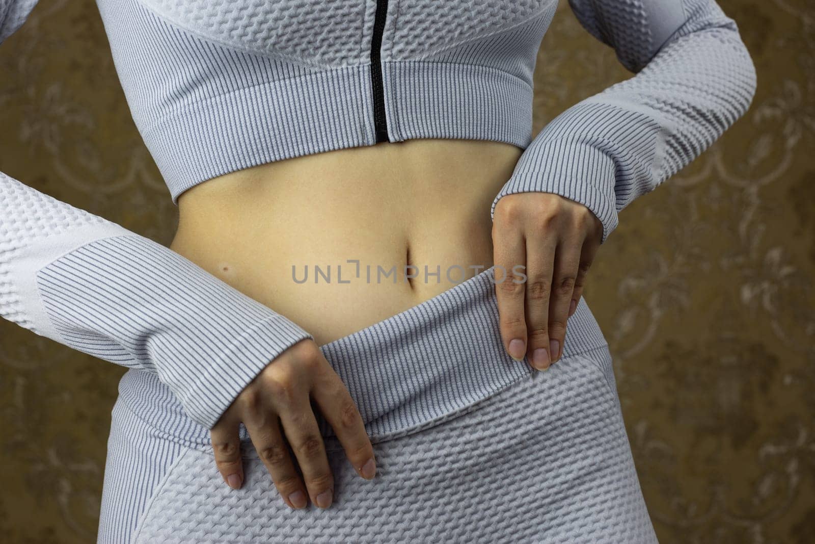 Girl in tracksuit for training adjusts her leggings at the waist with open navel by timurmalazoniia