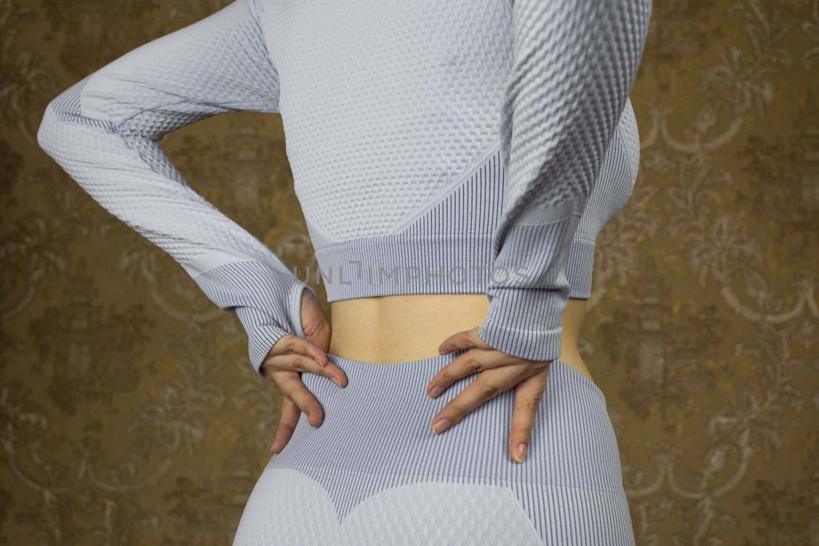 Girl pulls on sports leggings before training in gym, rear view of the waist of young skinny athletic girl