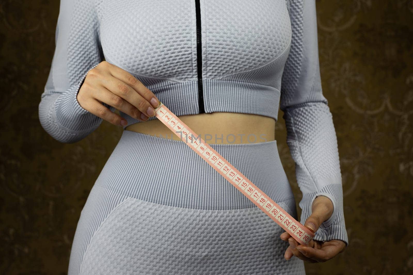 Sport girl in tight fitting suit holds tape for measuring her waist by timurmalazoniia