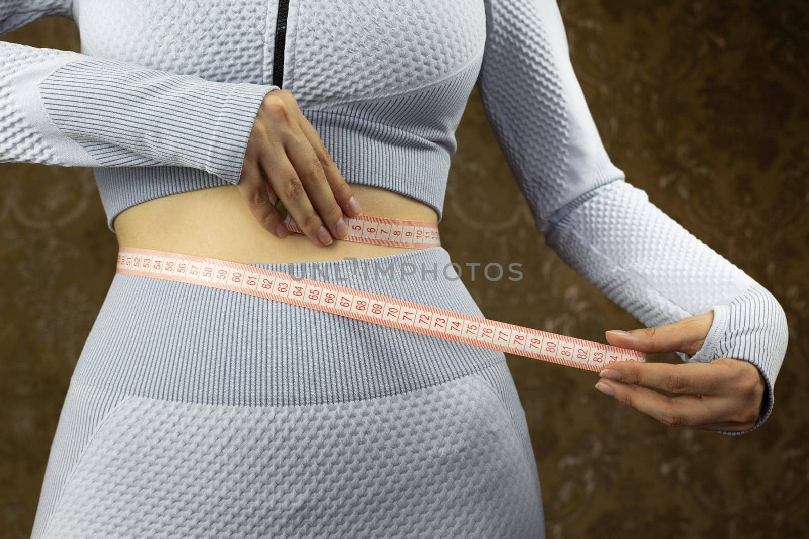 Girl in workout suit with cutout for her belly in gym measures her waist with special flexible tape, concept of sports and healthy lifestyle