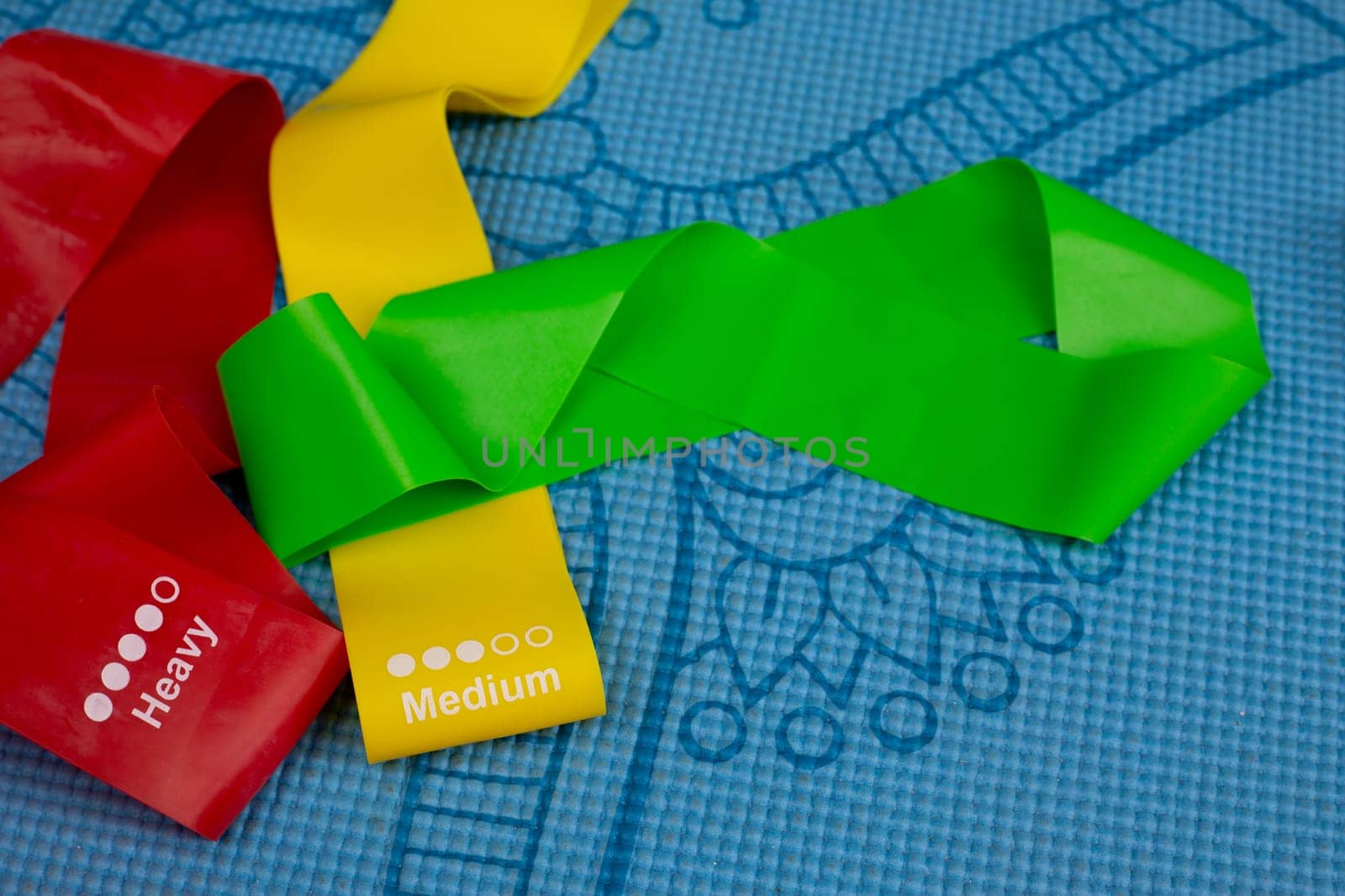 Multicolored rubber bands for sports of different hardness and degree of tension lie on sports mat, sport concept with equipment