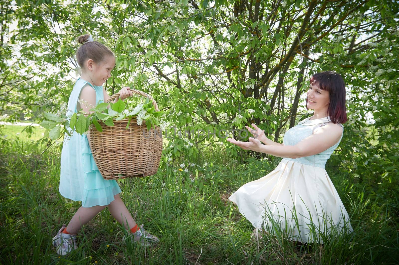 Happy mother and daughter enjoying rest, playing and fun on nature on a green lawn and with a blooming apple tree in the background. Woman and girl resting outdoors in summer and spring day by keleny