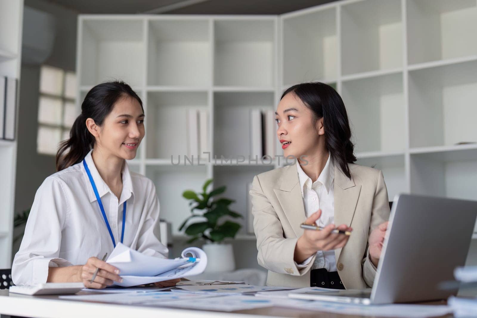 Two businesswomen engaged in teamwork, planning, and analysis discussion in a modern office environment.