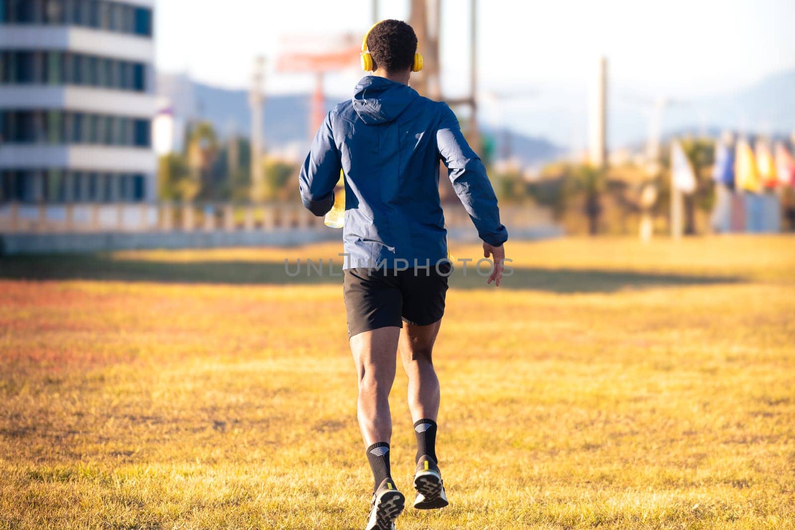 Rear view jockster running through city streets, with a bottle of water outdoors by mariaphoto3