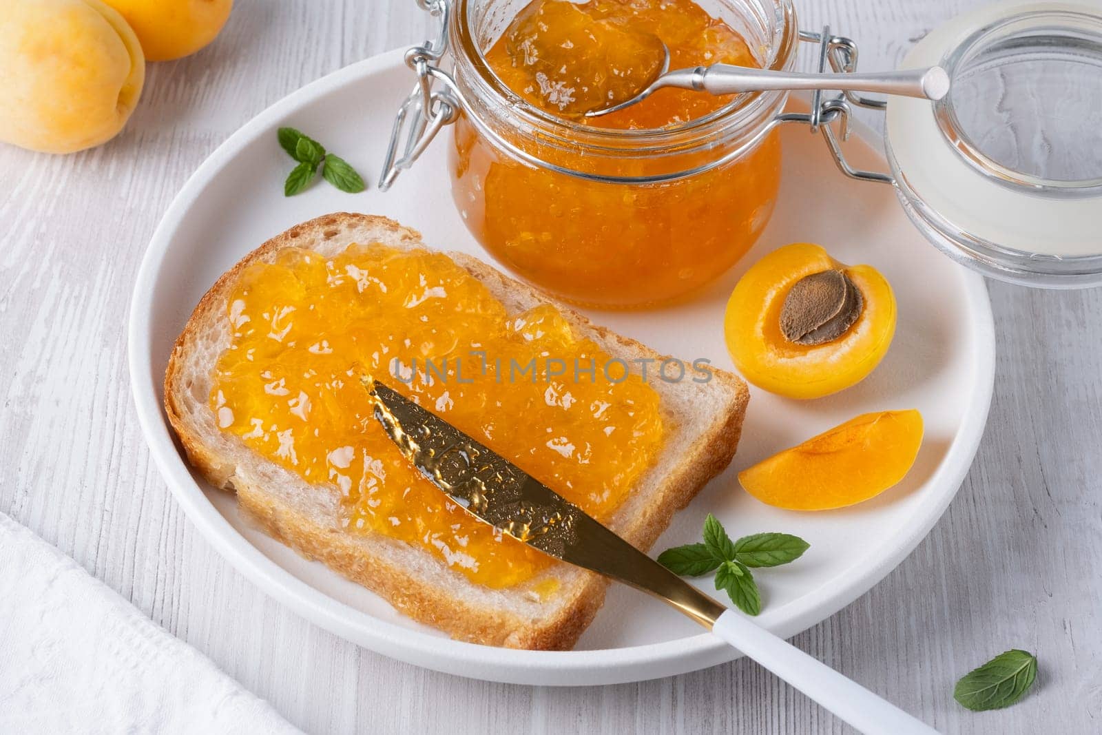 Apricot jam on bread in a white plate and a jar of apricot jam.
