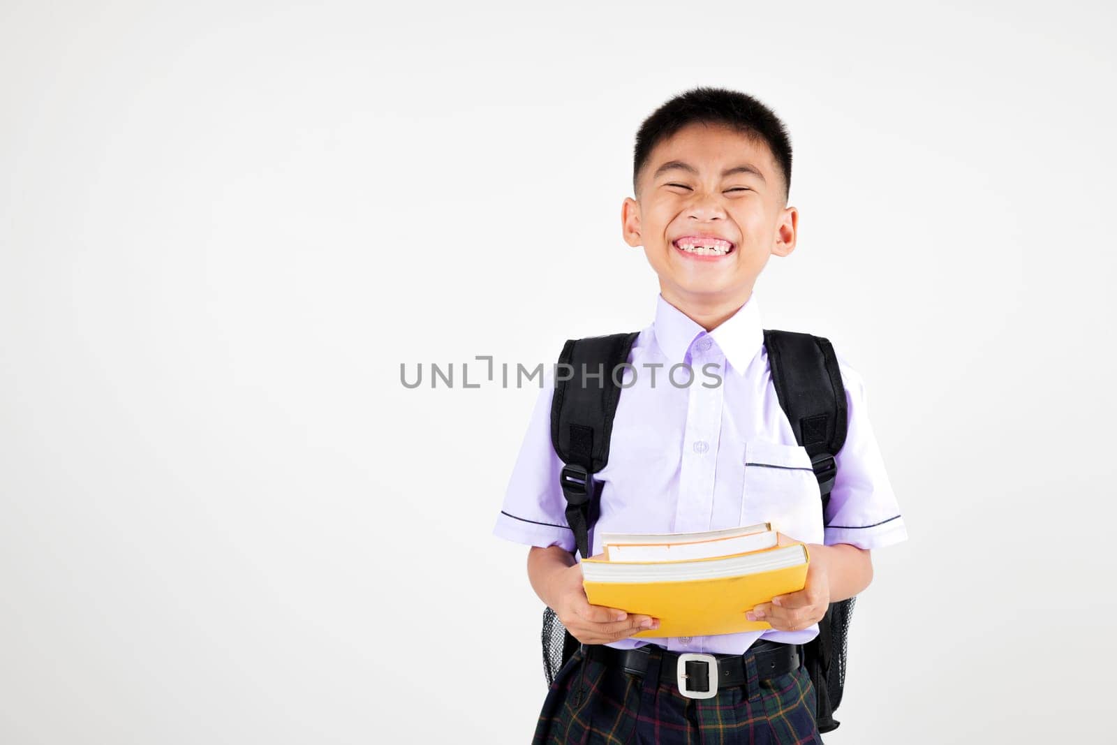 Portrait smile Asian little boy primary posing holding stack of books studio isolated white background, happy cute man kid wear school uniform and backpack learning and reading by Sorapop