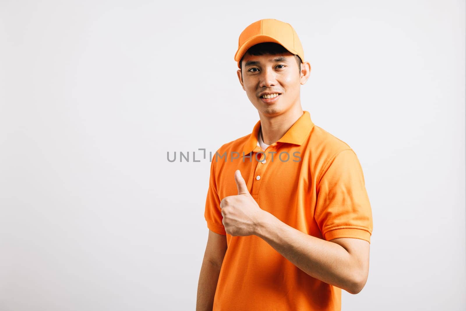 Portrait professional attractive delivery happy man standing he smile wearing orange t-shirt and cap uniform showing thumb up gesture looking to camera, studio shot isolated by Sorapop