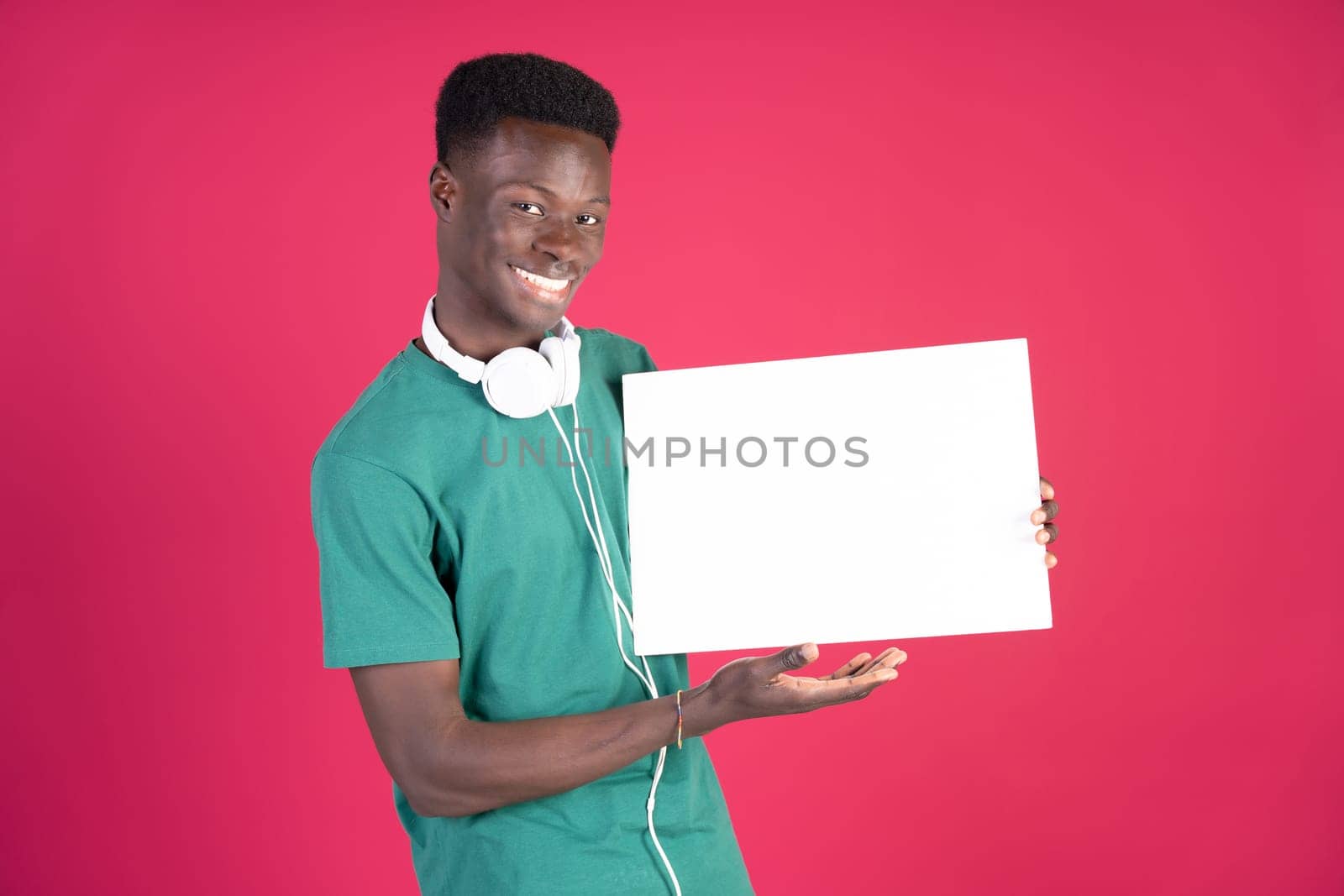 A young man wearing a green shirt and headphones is holding a white sign by Ceballos