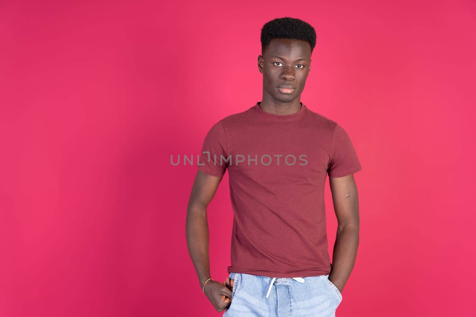 A man in a red shirt stands in front of a pink background by Ceballos