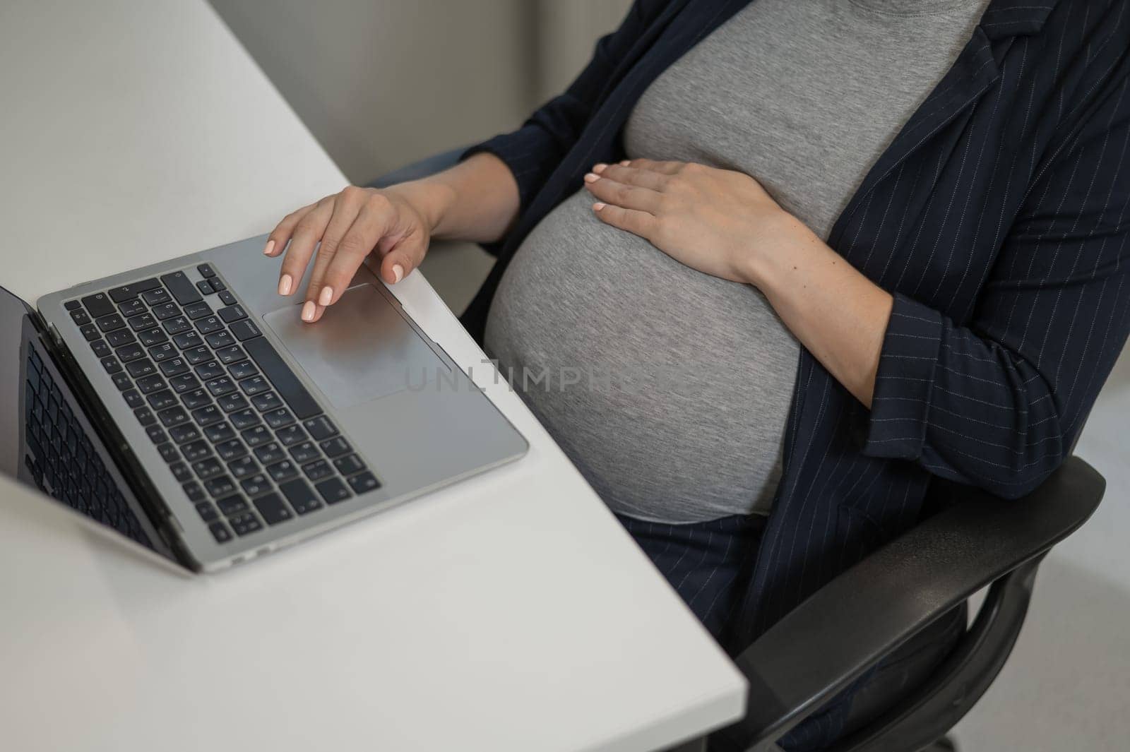 A pregnant woman works on a laptop in the office. Close-up of the tummy