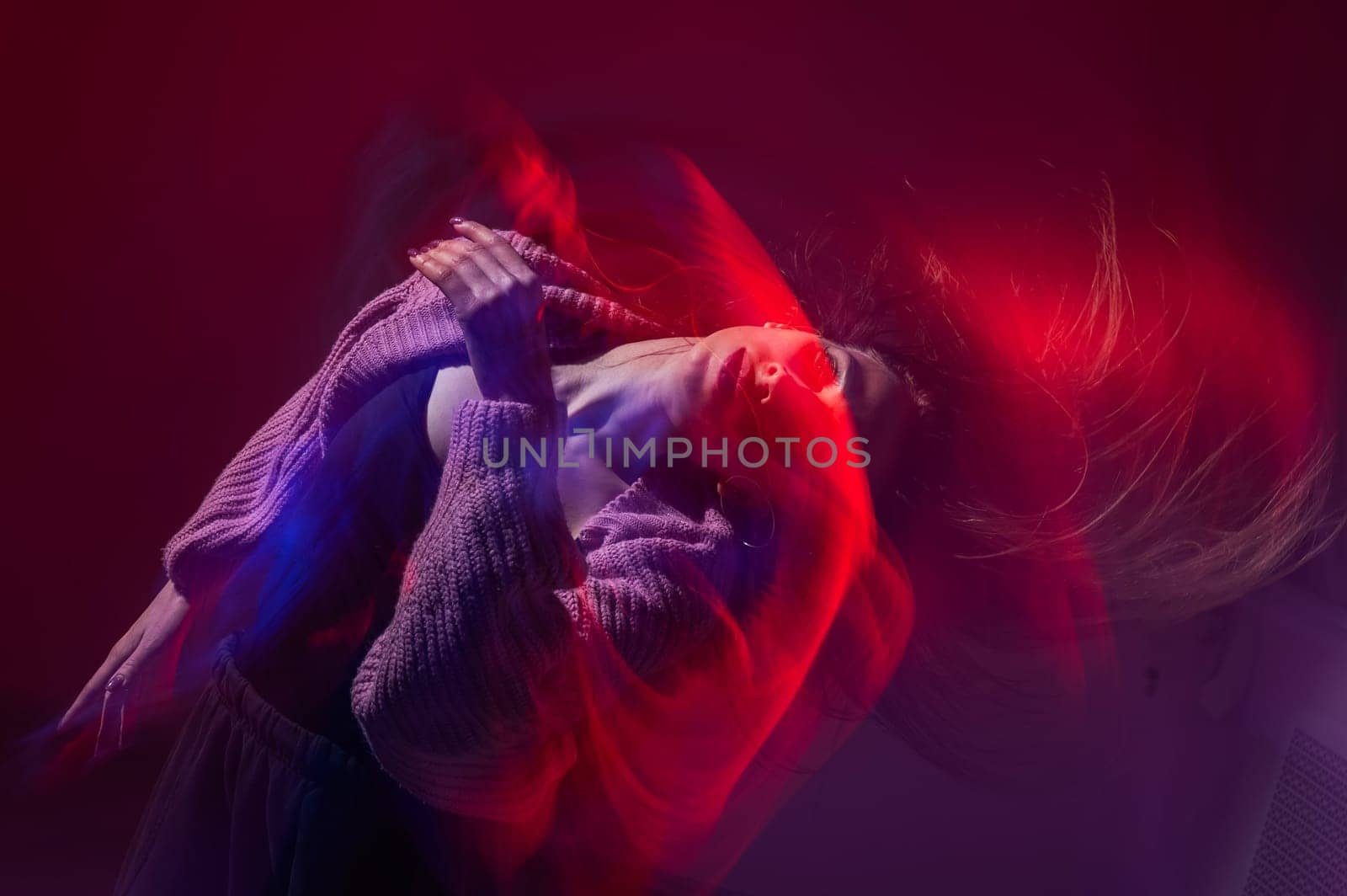 A young woman dances contemporary dances in blue and red light. Long exposure photo