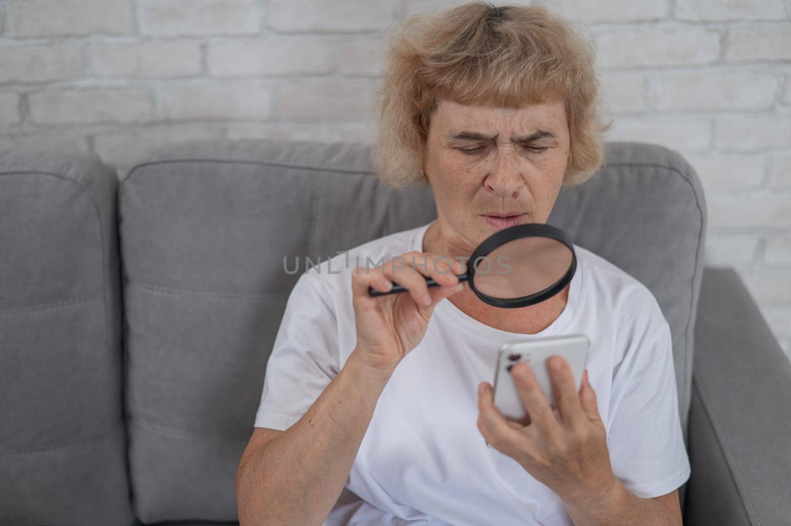 Elderly Caucasian woman with myopia and trying to read a message on a smartphone using a magnifying glass. by mrwed54