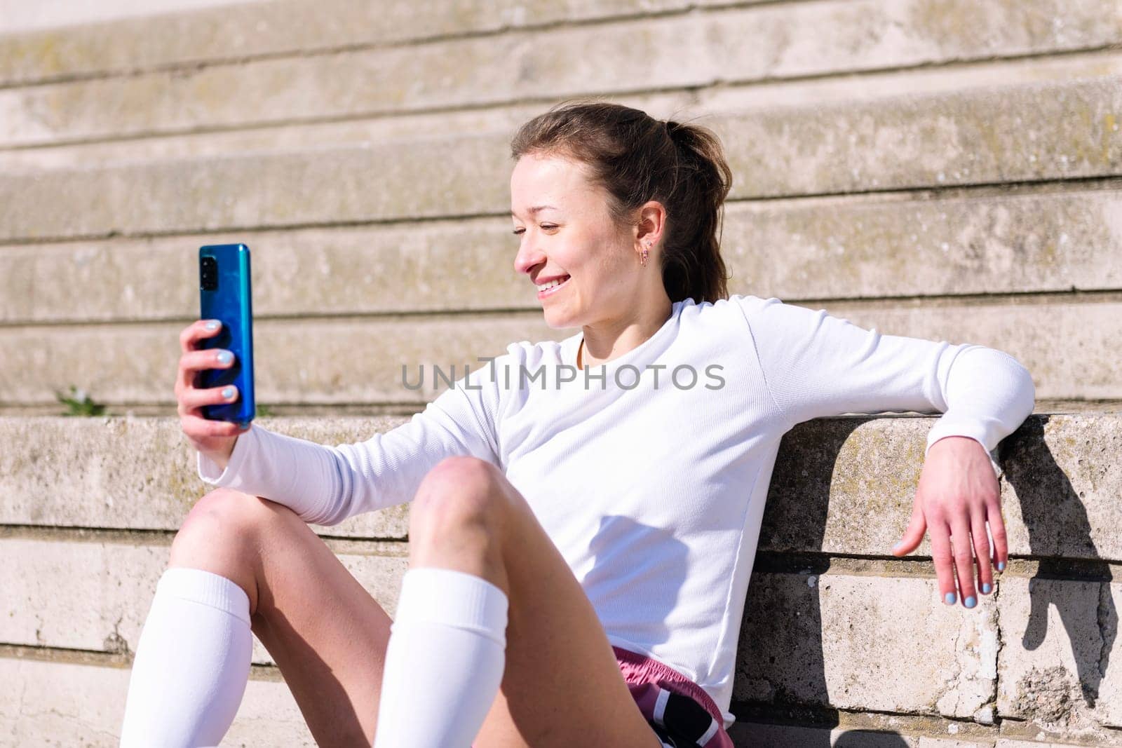 smiling sports woman resting sitting on the court using her mobile phone, concept of technology and urban sport lifestyle in the city